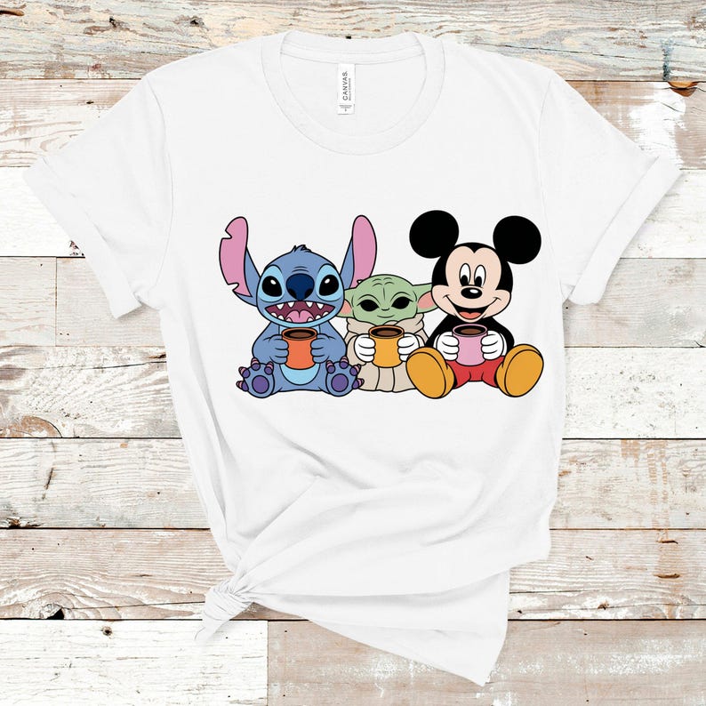 Puede incluir: Camiseta blanca con un gr&aacute;fico de Stitch, Baby Yoda y Mickey Mouse sosteniendo tazas de caf&eacute;.