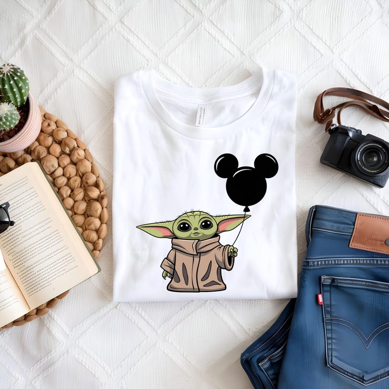 K&ouml;nnte beinhalten: Wei&szlig;es T-Shirt mit einer gr&uuml;nen Comicfigur, die einen schwarzen Mickey-Maus-Ballon h&auml;lt. Die Figur tr&auml;gt einen braunen Mantel.