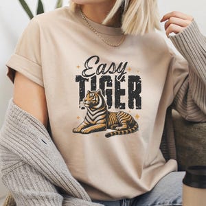 Könnte beinhalten: Ein beiges T-Shirt mit einem Vintage-Grafikdruck eines Tigers und dem Text "Easy Tiger".