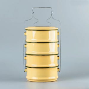 Peut inclure: Un porte-repas tiffin en émail jaune avec quatre compartiments empilés et une poignée en métal. Chaque section est bordée d'une bordure vert foncé. Le porte-repas est conçu pour transporter des aliments et a une esthétique classique et vintage.