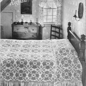 May include: A white crocheted bedspread with a floral pattern and fringe. The bedspread is on a bed with a wooden headboard. The word "Keepsake" is written in the top left corner of the image.