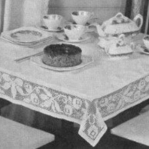 May include: A white tablecloth with a floral lace border, covering a dark wooden table. The table is set with a teapot, teacups, saucers, plates, and a cake. Chairs with white seats and striped backs surround the table.