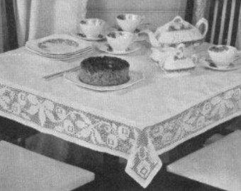 May include: A vintage white tablecloth with a floral lace border, set on a dark wooden table. The table is set with a teapot, teacups, saucers, plates, and a cake. The chairs have white seats and striped backs.