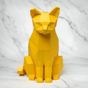 May include: A geometric, yellow cat sculpture. The cat is sitting upright with its ears perked up and tail extended. The sculpture is made of multiple flat planes, giving it a modern, angular appearance. The background is a white marble.