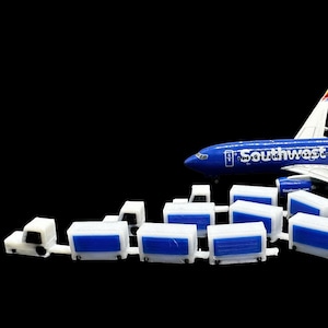 May include: A blue and white model airplane with the Southwest logo, accompanied by several white and blue cargo containers and trucks. The airplane has red, yellow, and orange accents on the tail. The background is black.