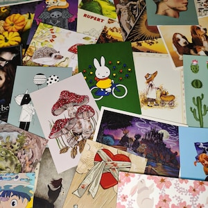 Könnte beinhalten: Eine Sammlung von Postkarten mit verschiedenen Illustrationen und Designs. Einige der Postkarten zeigen ein Kaninchen auf einem Fahrrad, einen Pilz, ein Herz mit einem Verband und ein Schloss im Hintergrund. Die Postkarten sind alle in verschiedenen Größen und Formen.