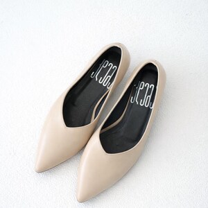 May include: A pair of beige pointed-toe flats. The shoes have a low-cut vamp and a black insole with white text. The shoes are made of a smooth material and are set against a white background.
