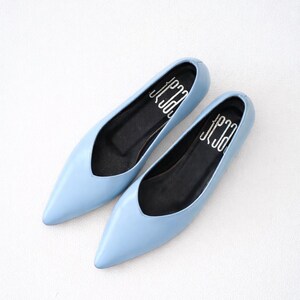 May include: A pair of light blue flats with pointed toes. The shoes have a low-cut vamp and black insoles with white text. The shoes are displayed on a white surface.