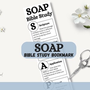 May include: A white SOAP Bible Study bookmark with text and a light blue banner that reads "SOAP BIBLE STUDY BOOKMARK". The bookmark includes sections for Scripture, Observation, Application, and Prayer. A pair of silver scissors and white flowers are also in the image.
