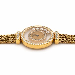 May include: A gold wristwatch featuring a round case encrusted with diamonds, a gold-toned dial with floating diamonds, and a multi-strand braided gold chain bracelet. The watch lugs are also set with diamonds, and the Chopard logo is visible.