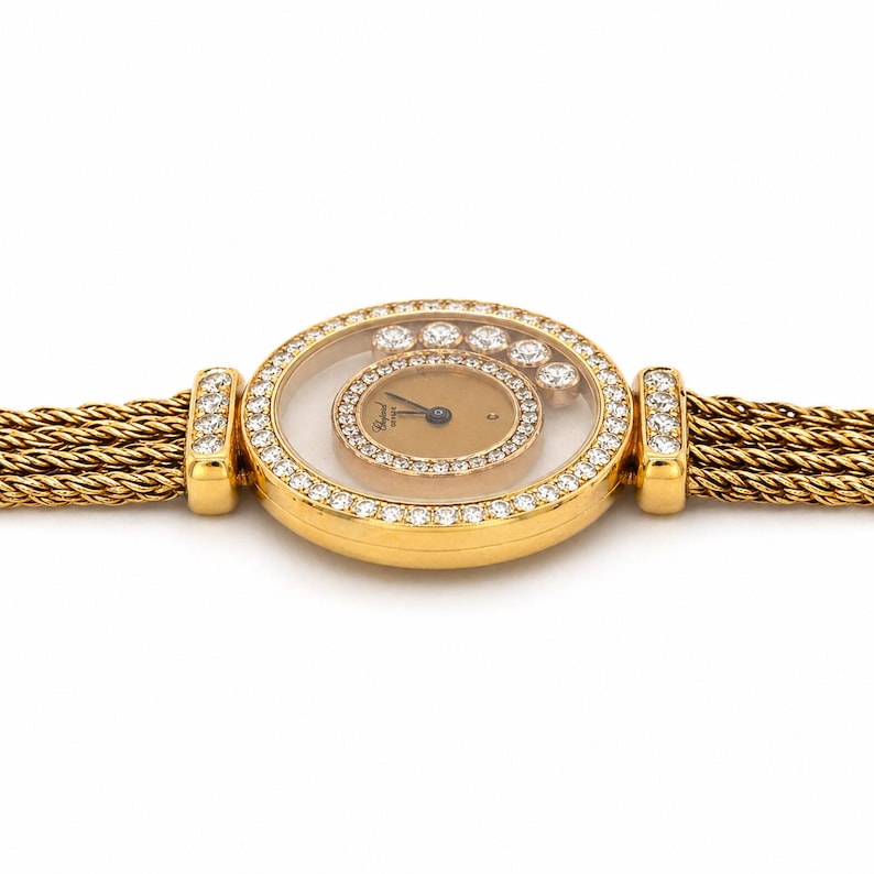 May include: A gold wristwatch featuring a round case encrusted with diamonds, a gold-toned dial with floating diamonds, and a multi-strand braided gold chain bracelet. The watch lugs are also set with diamonds, and the Chopard logo is visible.