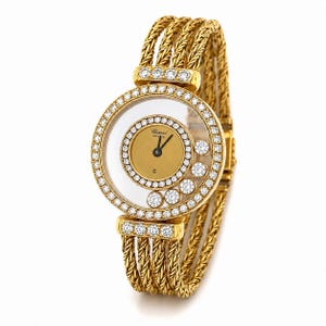 May include: A gold wristwatch featuring a round case with a diamond-encrusted bezel and five floating diamonds inside the crystal. The dial is gold with black hands and the Chopard Geneve logo. The band consists of multiple braided gold rope strands.