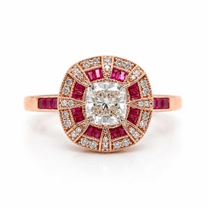 Könnte beinhalten: Ein Ring aus Roségold mit einem zentralen Diamanten im Kissenschliff, umgeben von einem Heiligenschein aus Baguette-Rubinen und runden Brillanten. Das Band ist mit im Kanal gefassten Rubinen verziert und weist durchgehend Milgrain-Kanten auf.