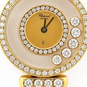 May include: A gold Chopard Geneve watch with a circular face featuring a solid gold center dial, black hands, and a bezel set with round diamonds. Five loose round diamonds float within the clear space between the dial and the outer diamond-encrusted rim.