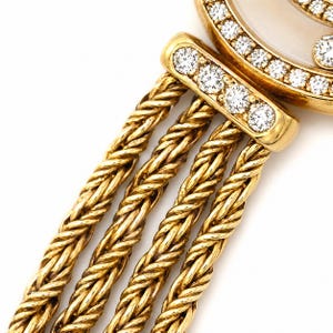 May include: A gold watch featuring a round case with a mother-of-pearl dial and a bezel set with round diamonds. The watch has a triple-strand braided gold chain bracelet attached to a diamond-encrusted lug, showcasing a polished metallic finish.
