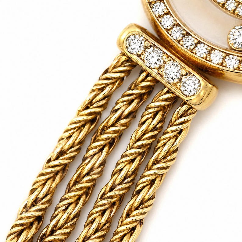 May include: A gold watch featuring a round case with a mother-of-pearl dial and a bezel set with round diamonds. The watch has a triple-strand braided gold chain bracelet attached to a diamond-encrusted lug, showcasing a polished metallic finish.