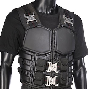 May include: Black tactical vest with multiple pockets and silver buckles. The vest has padded sections and a front zipper. Red stitching accents the straps and edges of the vest, giving it a rugged appearance.