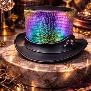 May include: A black top hat with a band featuring a colourful, iridescent, crocodile-textured pattern. The hat has a black brim and is decorated with small silver studs and a purple gem. It is displayed on a marble surface.