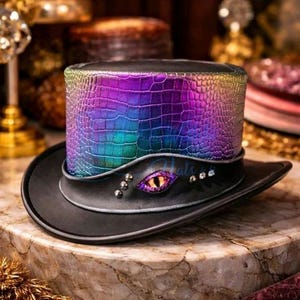 May include: A black top hat with a vibrant, iridescent, crocodile-effect band. The hat has an eye-shaped embellishment with a yellow iris and purple details, plus silver studs. The brim is black.