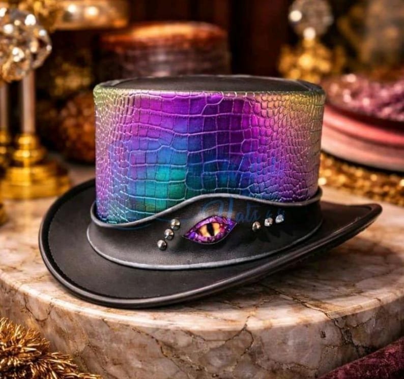 May include: A black top hat with a vibrant, iridescent, crocodile-effect band. The hat has an eye-shaped embellishment with a yellow iris and purple details, plus silver studs. The brim is black.