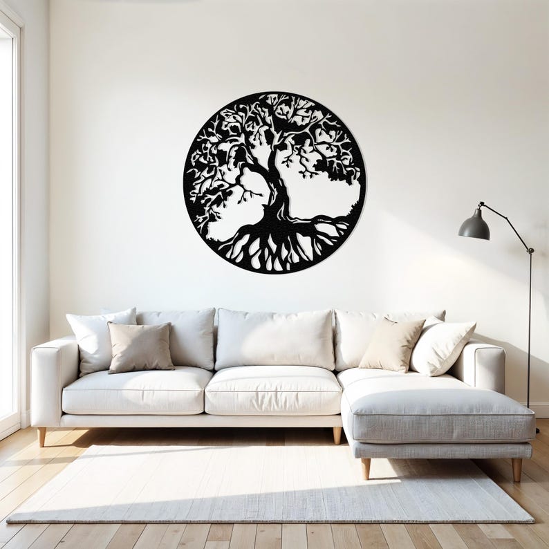 May include: A black metal wall art sculpture of a tree of life with intricate branches and roots. The sculpture is circular and is mounted on a white wall above a white couch.
