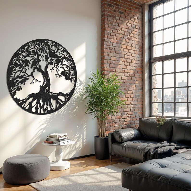 May include: Black metal tree of life wall decor in a circular shape, hanging on a white wall in a living room setting. The tree has intricate branches and roots. The wall decor is in front of a black leather sofa and a potted plant.