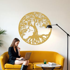 May include: A yellow wooden tree of life wall decor with intricate branches and roots. The decor is hanging on a white wall in a living room setting with a yellow couch and a lamp.