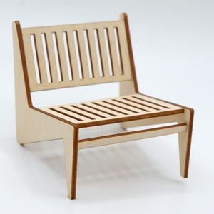 May include: A miniature chair constructed from light-coloured wood with a slatted backrest and a slatted seat. The piece features clean, angular lines and dark brown edges along the frame, showcasing a simple, flat-pack style assembly design.