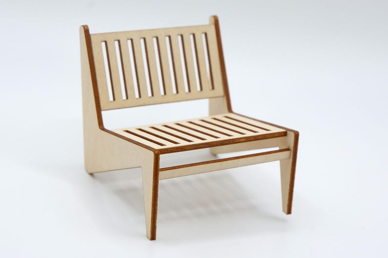 May include: A miniature chair constructed from light-coloured wood with a slatted backrest and a slatted seat. The piece features clean, angular lines and dark brown edges along the frame, showcasing a simple, flat-pack style assembly design.