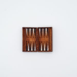 May include: A wooden backgammon board, featuring a dark brown frame and a playing surface with alternating white and brown triangles. The board is open, revealing the game's layout.