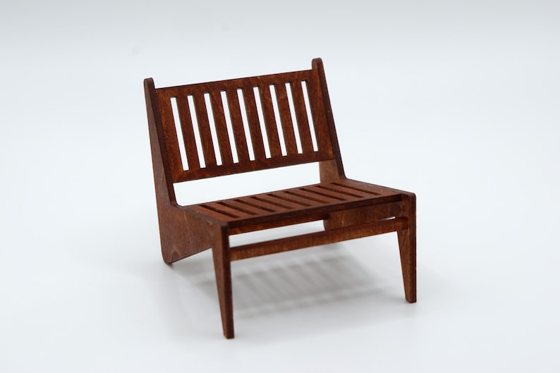 May include: A miniature chair constructed from brown wood, featuring a slatted backrest and a slatted seat. The chair has four legs and a low-profile design with a visible wood grain texture throughout the entire structure of the piece.