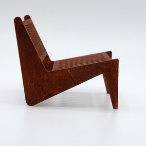 May include: A miniature chair constructed from dark brown wood, featuring a slatted backrest and a slatted seat. The chair has a low-profile, angled design with a continuous side frame that forms both the back support and the front legs.