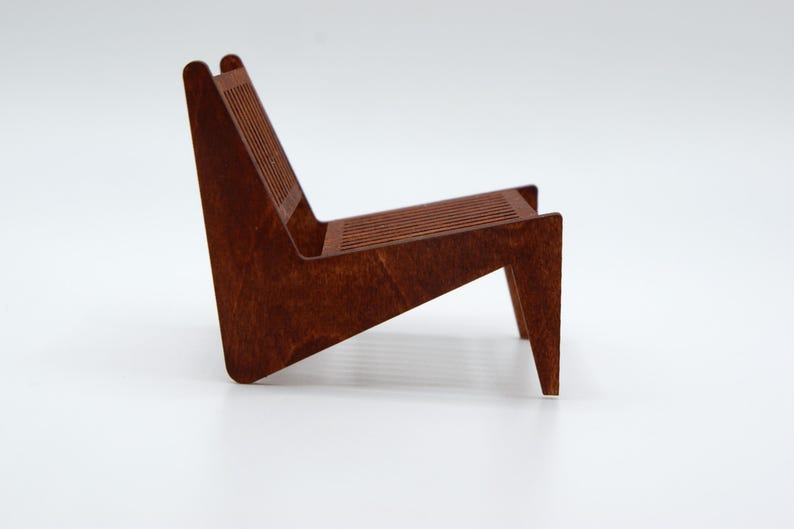 May include: A miniature chair constructed from dark brown wood, featuring a slatted backrest and a slatted seat. The chair has a low-profile, angled design with a continuous side frame that forms both the back support and the front legs.
