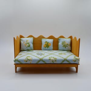 May include: A miniature wooden sofa with a scalloped back and armrests. The cushions and seat are covered in a light blue fabric with a floral pattern. Three matching throw pillows complete the set, creating a charming dollhouse furniture piece.