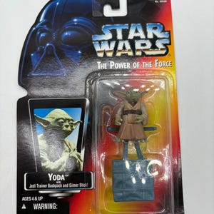 May include: A Star Wars "The Power of the Force" action figure of Yoda with a Jedi Trainer Backpack and Gimer Stick. The figure is in a clear plastic package with a colorful cardboard backing featuring Darth Vader and the Star Wars logo.