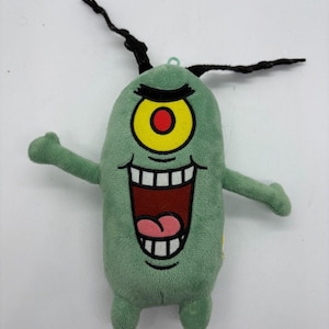 May include: A green Plankton plush toy from Spongebob Squarepants. The toy has a large yellow eye with a red centre, a wide open mouth, and black antennae. The plush is designed to resemble the cartoon character.