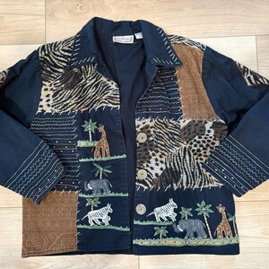 May include: A navy blue button-down jacket featuring a patchwork design with animal print panels, including zebra and leopard patterns. The jacket displays embroidered scenes of giraffes, elephants, and zebras among palm trees, with white stitching.