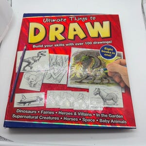 May include: A red instructional drawing book titled Ultimate Things to Draw with a purple pencil on the cover. The cover features illustrations of a dinosaur, elephant, space shuttle, and dragon, with text listing categories like Dinosaurs, Fairies, and Horses.