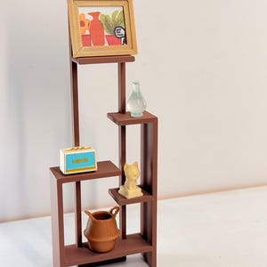 May include: A brown miniature display shelf with multiple levels, holding a framed picture, a small vase, a radio with the word "MUSIC", a cat figurine, and a woven basket. The shelf is a decorative item.