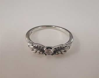 May include: A silver-toned ring featuring a central round clear gemstone flanked by two detailed wing-shaped motifs. The band is smooth and polished, with the wing designs extending from the center setting to create a symmetrical appearance.