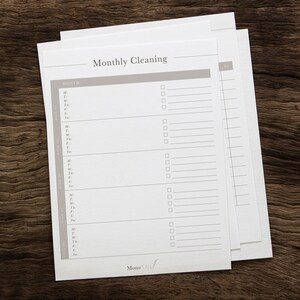 Op de afbeelding: Een printbare maandelijkse schoonmaakchecklist met een grijze kop en witte tekst die "Maandelijkse schoonmaak" luidt. De checklist heeft een kolom voor de datum en een kolom voor taken.