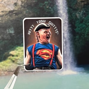 May include: A rectangular sticker featuring a character in a blue Superman shirt with red suspenders and a pirate hat. The sticker has the text "HEY YOOOU GUUYYYS!!" in a semi-circle around the character's head. The background is a waterfall.