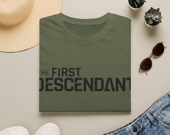 Könnte beinhalten: Ein olivgrünes Kurzarm-T-Shirt mit dem schwarzen Schriftzug THE FIRST DESCENDANT auf der Brust. Das T-Shirt wird zusammen mit einem Strohhut, einer Sonnenbrille, weißen Turnschuhen und einer blauen Jeanshose präsentiert.