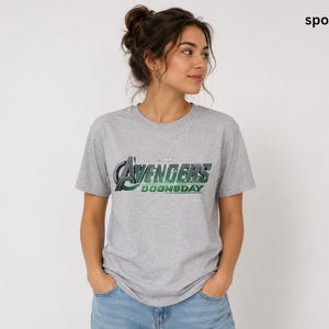 K&ouml;nnte beinhalten: Ein sportgraues Kurzarm-T-Shirt mit dem Schriftzug Avengers Doomsday, der in einem metallischen Gr&uuml;n-Silber-Verlauf auf der Brust gedruckt ist. Das Shirt hat einen Rundhalsausschnitt und eine Standardpassform im l&auml;ssigen Design.