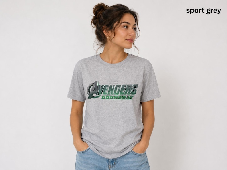 K&ouml;nnte beinhalten: Ein sportgraues Kurzarm-T-Shirt mit dem Schriftzug Avengers Doomsday, der in einem metallischen Gr&uuml;n-Silber-Verlauf auf der Brust gedruckt ist. Das Shirt hat einen Rundhalsausschnitt und eine Standardpassform im l&auml;ssigen Design.