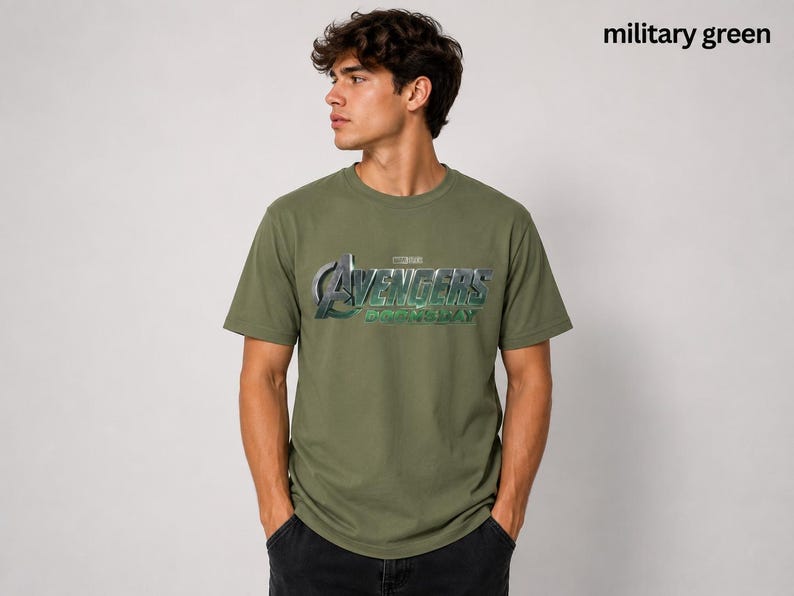 K&ouml;nnte beinhalten: Ein milit&auml;rgr&uuml;nes Kurzarm-T-Shirt mit dem metallisch silbernen und gr&uuml;nen Avengers Endgame-Logo auf der Brust. Das Shirt verf&uuml;gt &uuml;ber einen Rundhalsausschnitt und eine Standardpassform, die das ikonische Film-Branding als Grafikdesign zeigt.