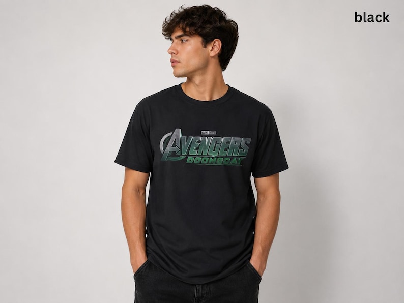 K&ouml;nnte beinhalten: Ein schwarzes kurz&auml;rmeliges T-Shirt mit einem Grafikdruck auf der Brust, der den Text Avengers Doomsday in einer metallisch silbernen und gr&uuml;nen Schrift zeigt. Das T-Shirt hat einen Rundhalsausschnitt und eine Standardpassform, mit dem Wort black.