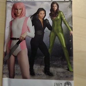 May include: Simplicity sewing pattern number 8670, size US 16-24, talla euro 42-50, taille fr 44-52. The pattern features three women wearing different costumes. One woman is wearing a pink and white costume with a belt and a knife. Another woman is wearing a black costume with a belt. The third woman is wearing a green costume with a zip.