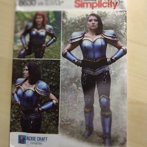 May include: A Simplicity sewing pattern for a blue and gold costume with a metallic finish. The pattern is for a woman's costume and includes a bodice, trousers, and leg armour. The pattern is labelled "Jackie Craft Cosplay".