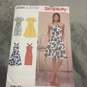 May include: Simplicity sewing pattern number 6594 for a dress. The pattern includes four different styles: a sleeveless dress with a halter neckline, a sleeveless dress with a scoop neckline, a sleeveless dress with a scoop neckline and a floral print, and a sleeveless dress with a scoop neckline and a polka dot print. The pattern is for sizes UK 14-22, Euro 40-48, and French 42-50.